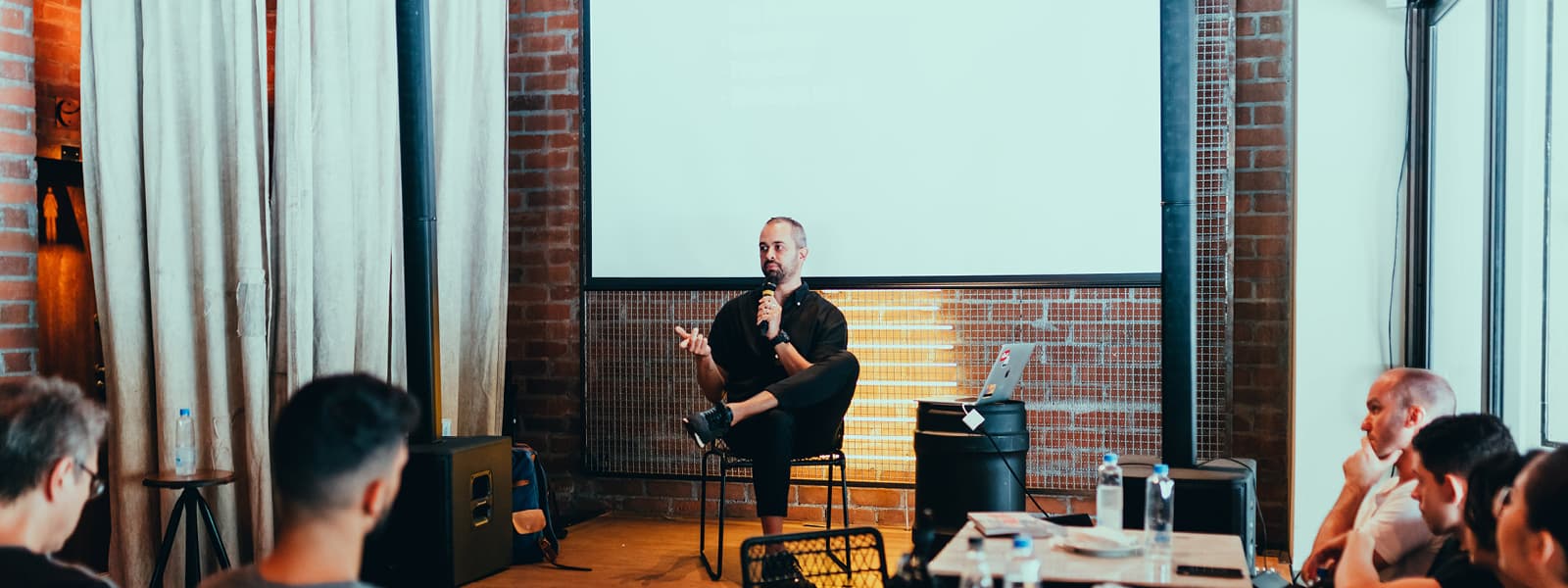 A man sitting in a chair speaking on a microphone as members in a meeting listen.