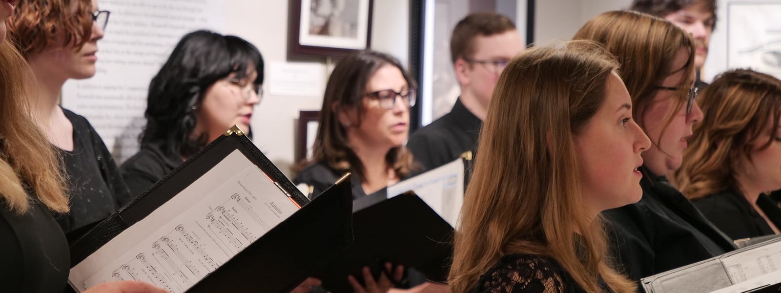 Students in a choir holding sheet music and singing.