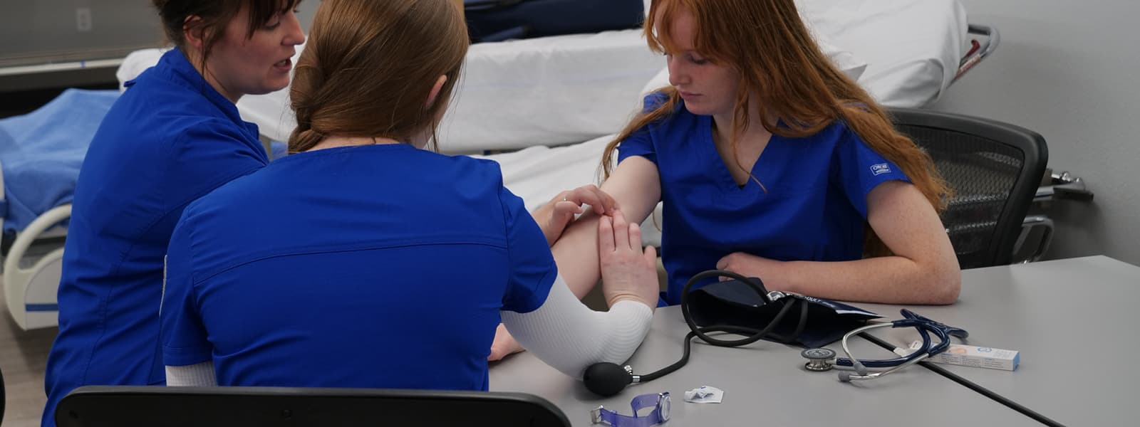 A nursing instructor is showing a student nursing techniques on another student. 