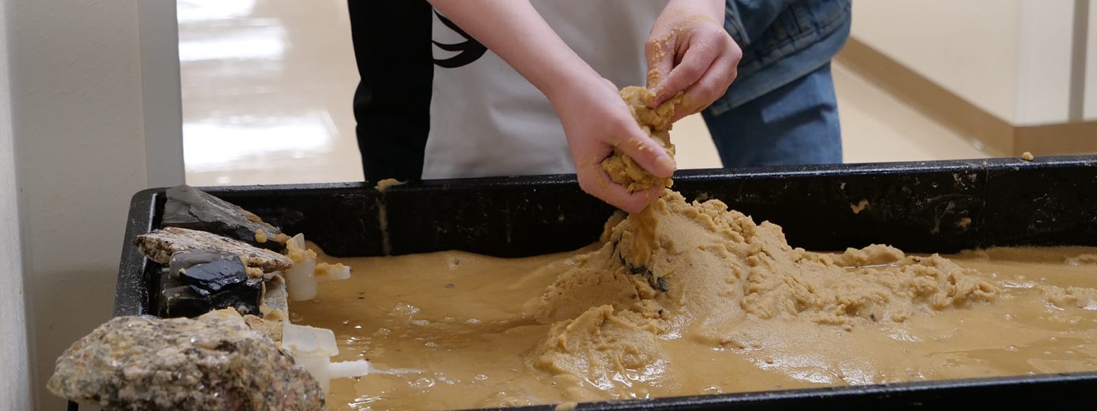 A student is working with his hands in dirt in a classroom.