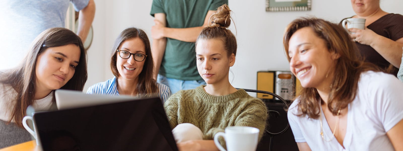 A group of students gathered around a laptop watching something.