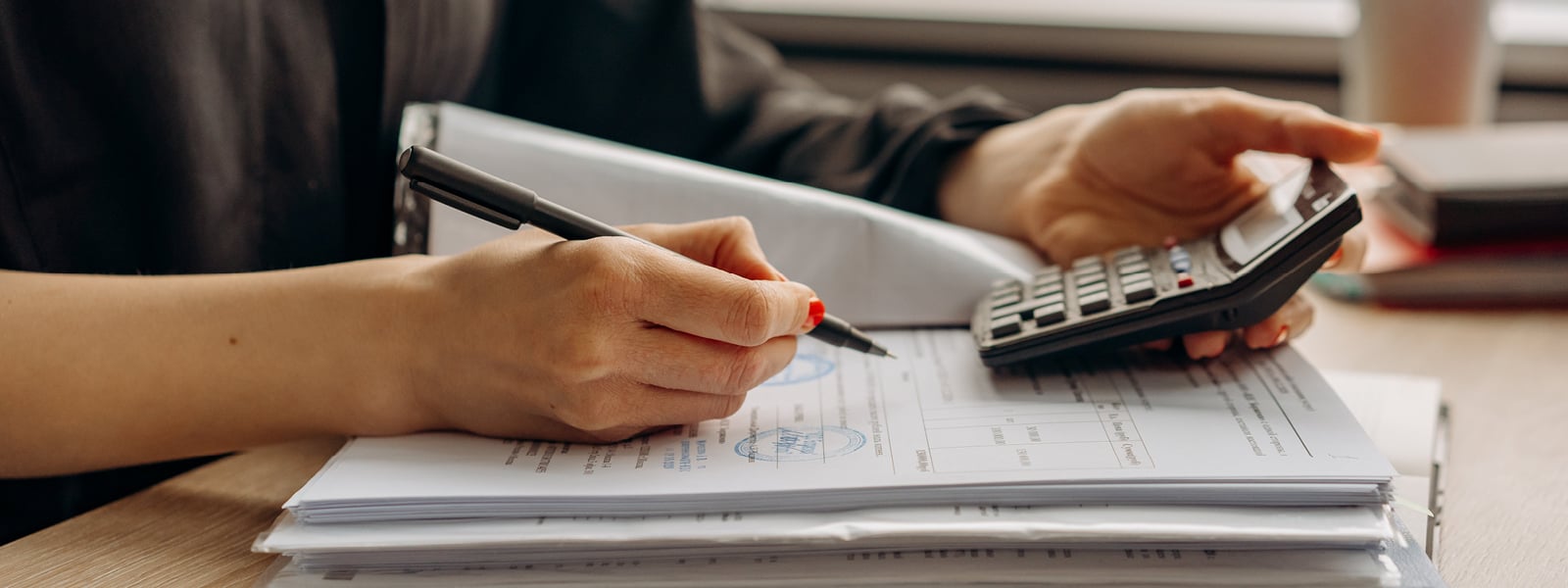 A person is writing in a notebook while using a calculator to do a calculation.