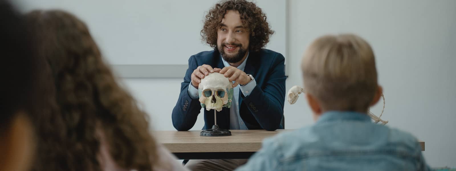 A professor is using a model skull to demonstrate to a classroom.