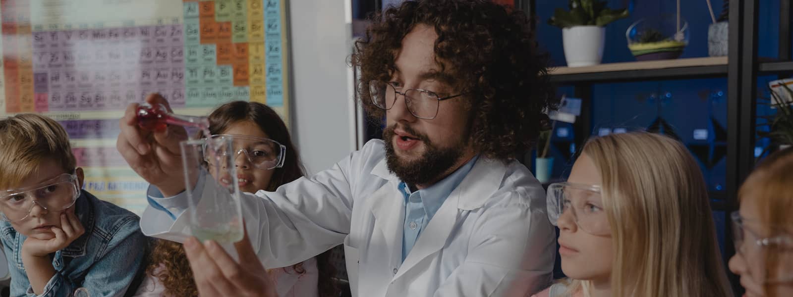 A professor is performing a scientific experiment with a beaker in a clasroom.