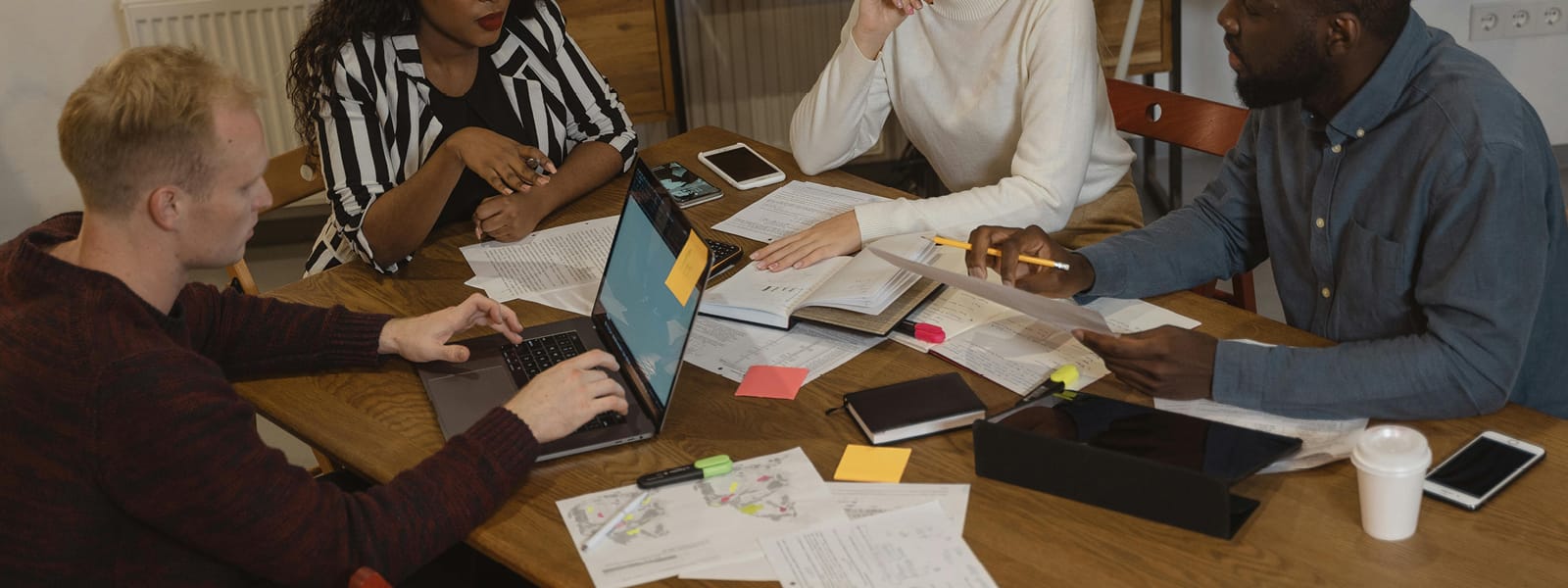 A group of students study at a table full of papers, books and a laptop. 