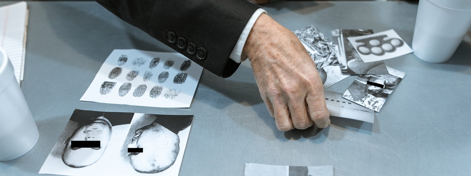 A man picks up crime photographs that are sitting on a table along with fingerprint samples.