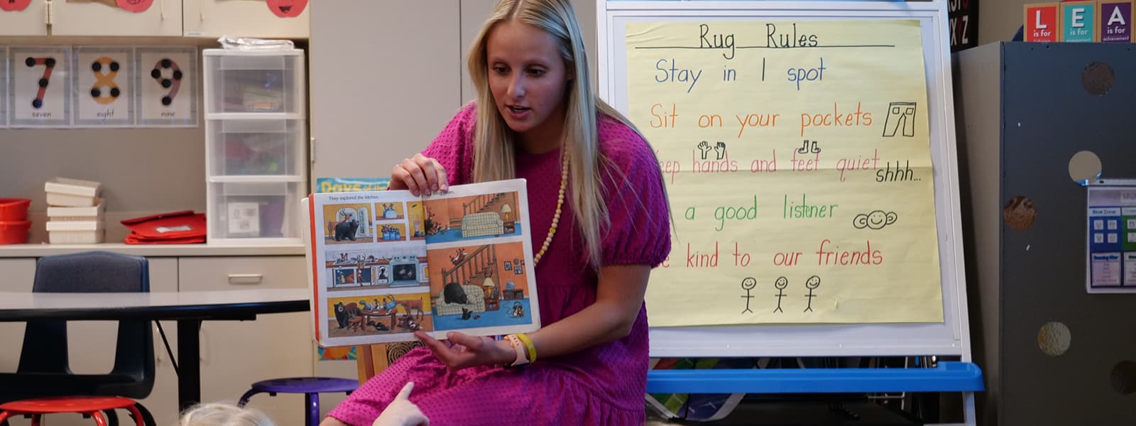 A woman reads a book to an elementary classroom.