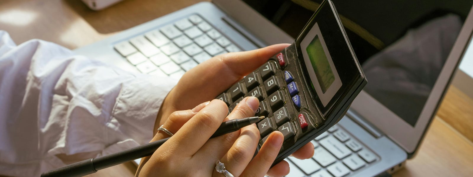 A student using a calculator while sitting in front of a laptop. 