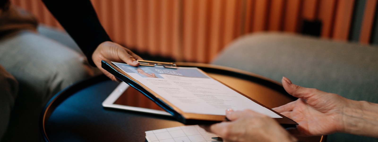 A person handing someone else a form on a clipboard. 