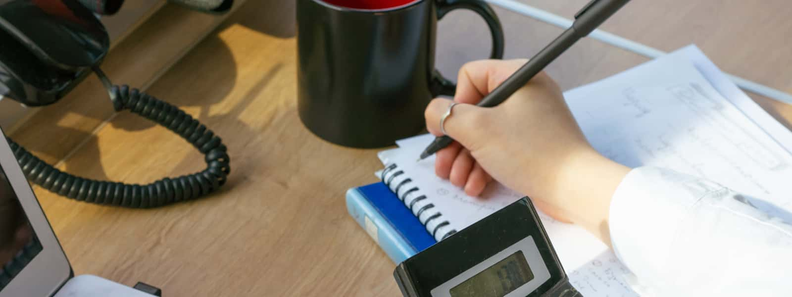 A person writes in a notebook at a business desk.