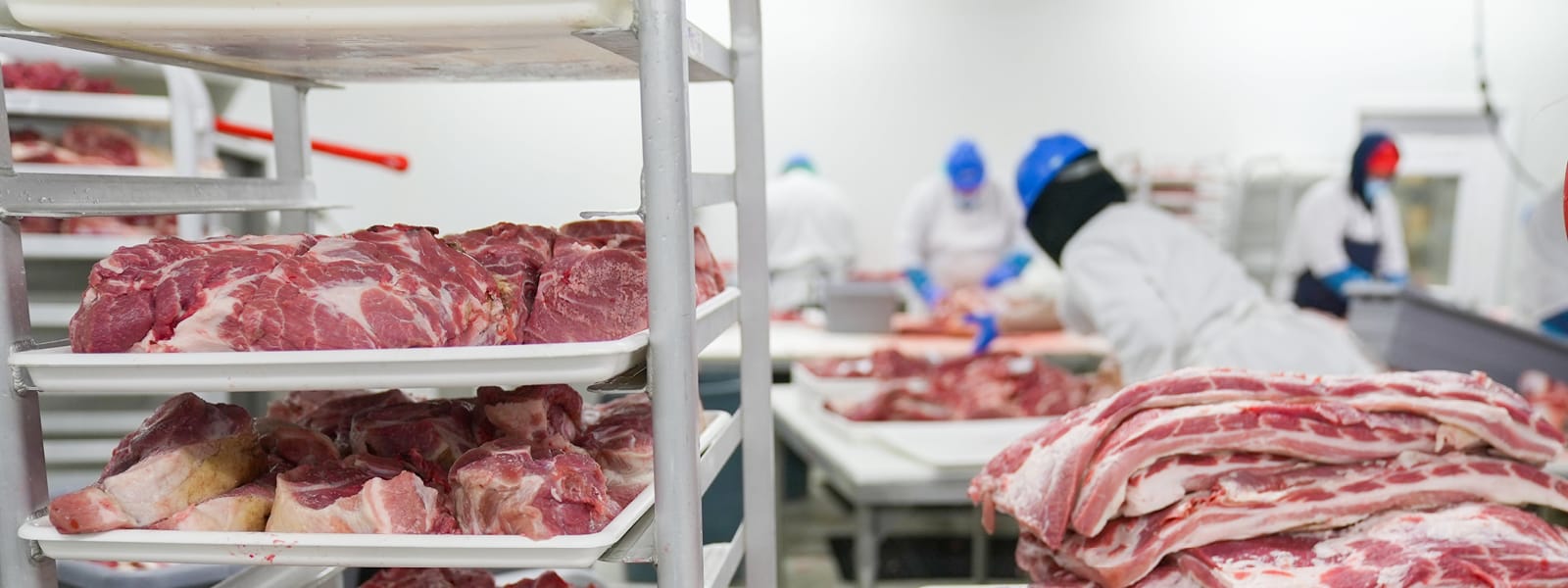 Various trays holding meat with workers in the background.