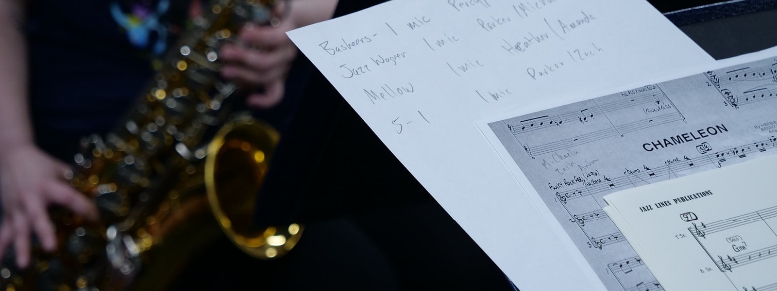 Sheet music and a student playing a saxophone in the background.