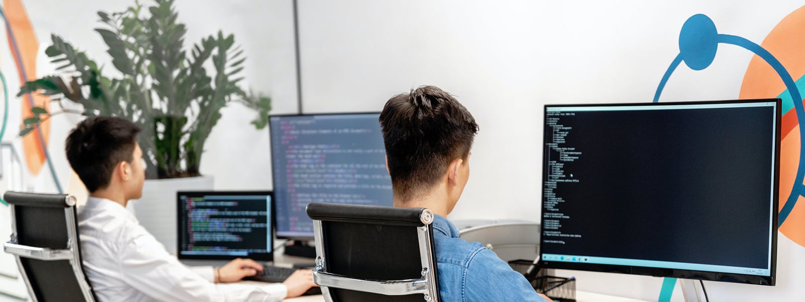 Two men work in front of multiple computer screens.